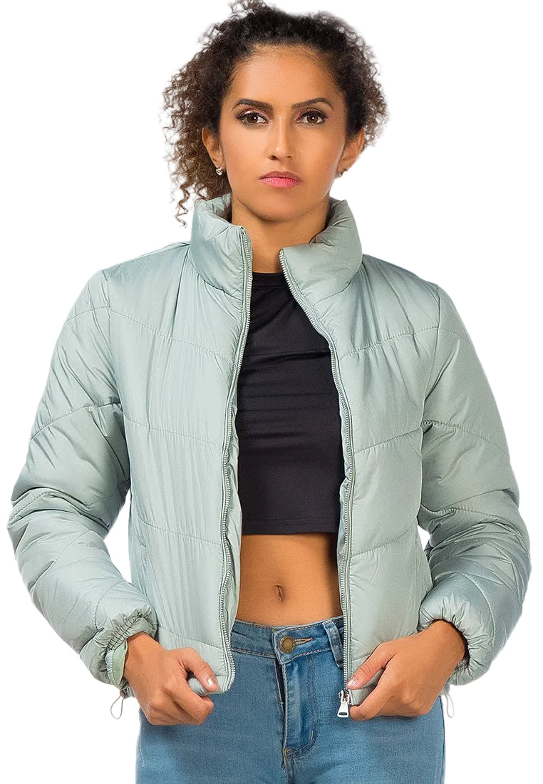 Woman wearing a light green puffer jacket over a black top and blue jeans on a white background