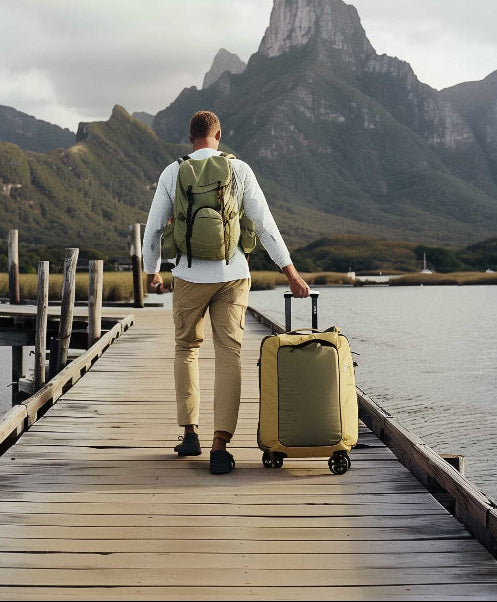 man walking down long pier with luggage on wheels and backpack on.
